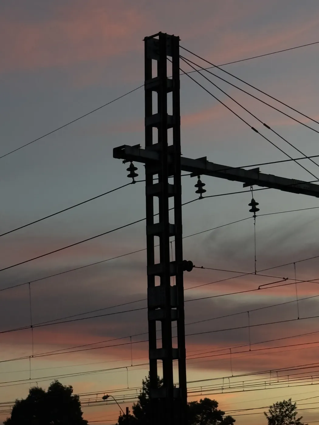 Poste del tendido eléctrico ferroviario recortado contra un atardecer